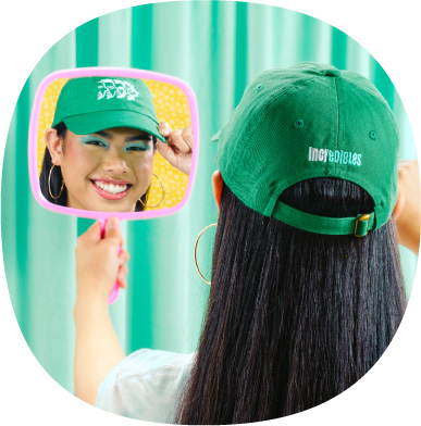Girl smiling in a handheld mirror with a green hat